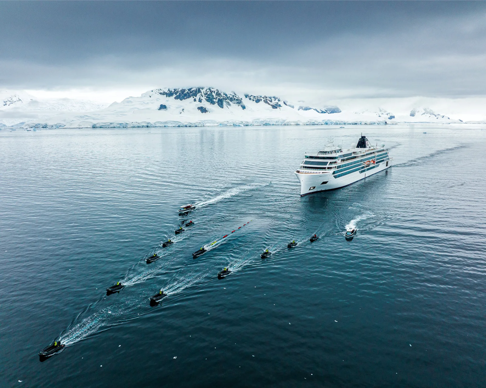 Viking expedition ship flanked by a fleet of Zodiacs in Antarctic waters with snow-capped mountains